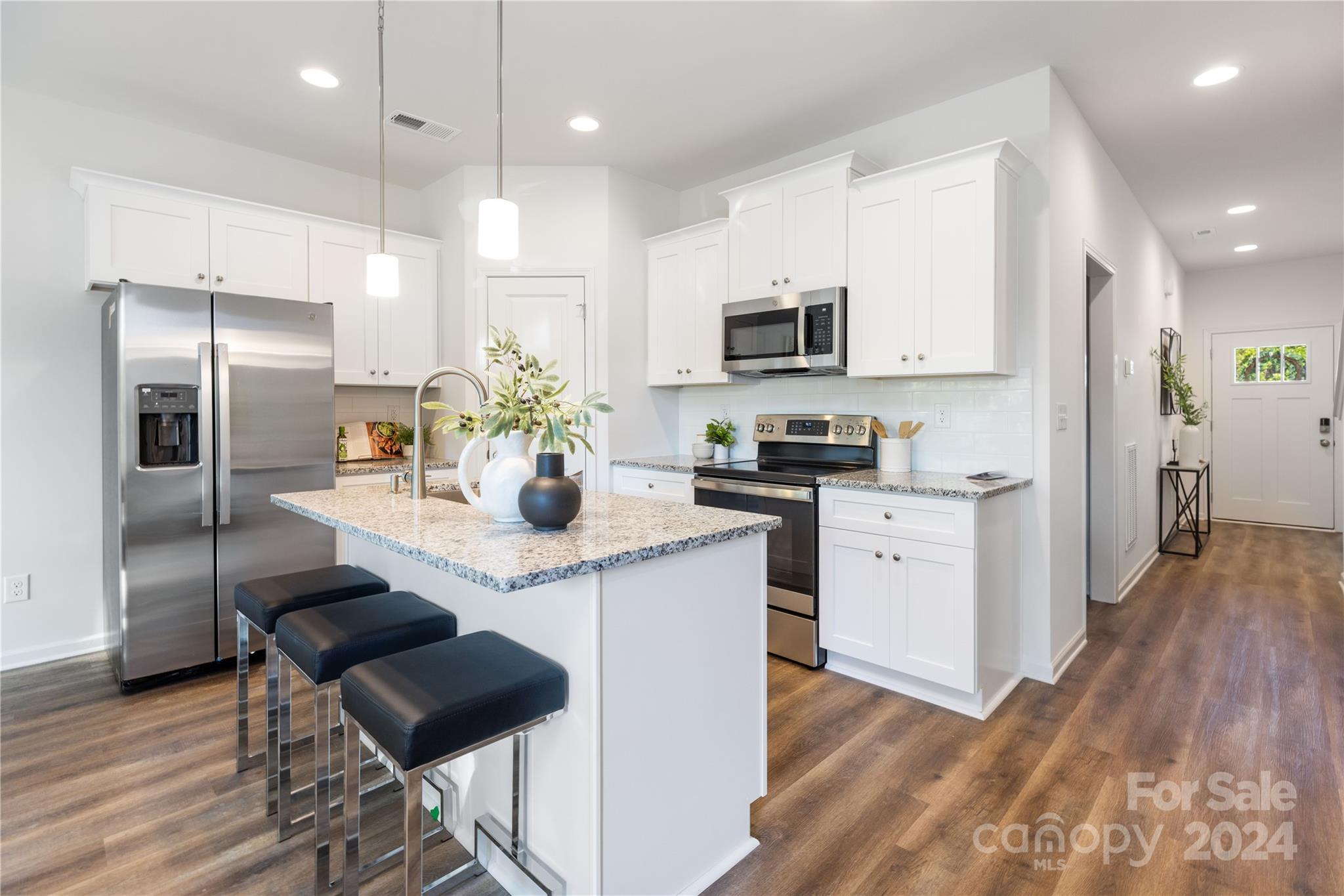 a kitchen with stainless steel appliances kitchen island granite countertop a refrigerator a sink dishwasher a stove and white cabinets with wooden floor