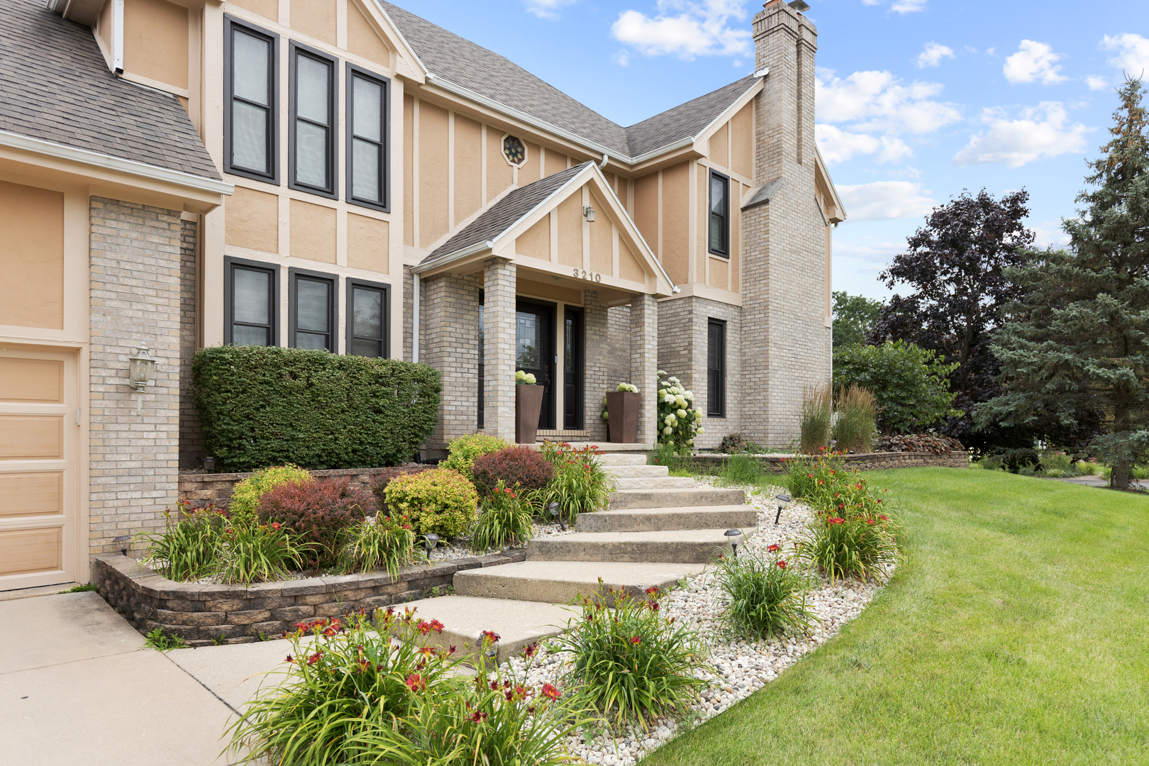 a view of a house with brick walls plants and large tree