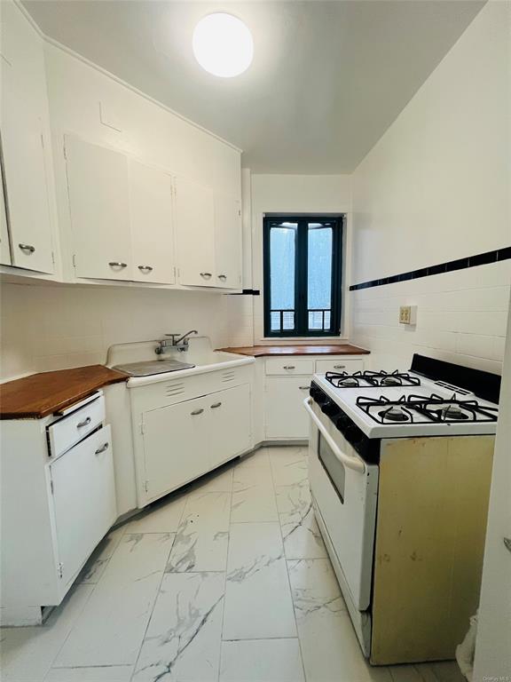 Kitchen with tasteful backsplash, white cabinetry, sink, and white range with gas stovetop