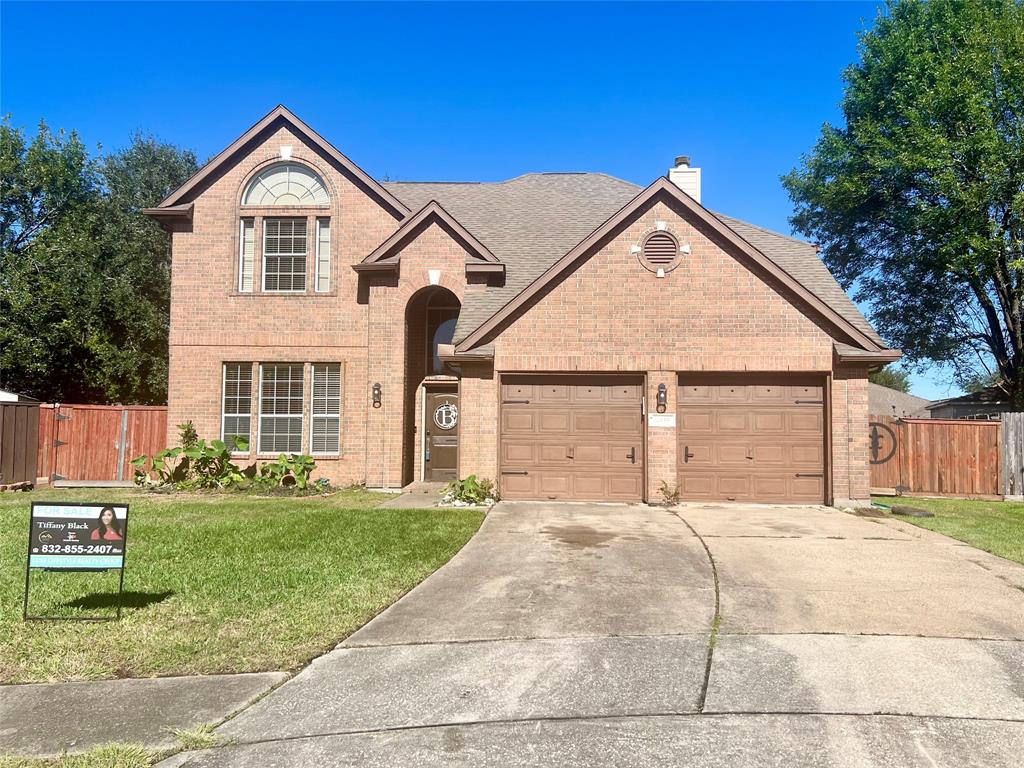 The photo showcases a two-story brick house with a steeply pitched roof and an attached garage. There's a well-maintained lawn and a wooden privacy fence on one side. The home features a traditional design and is situated in a suburban neighborhood.