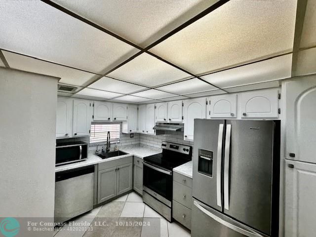 a kitchen with stainless steel appliances a refrigerator a stove a sink and white cabinets