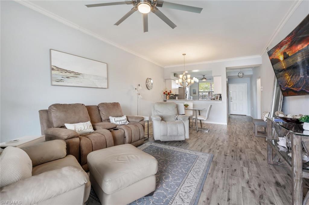 Living room with ceiling fan with notable chandelier, light hardwood / wood-style flooring, and ornamental molding