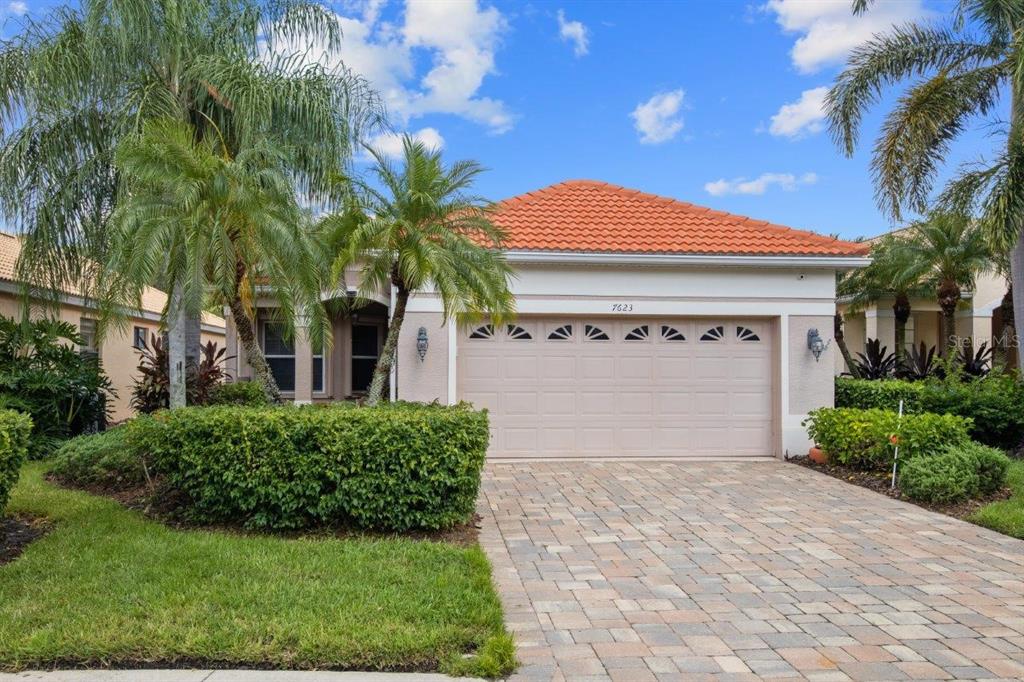 Front elevation showing the paver driveway, tile roof, and tropical landscaping.