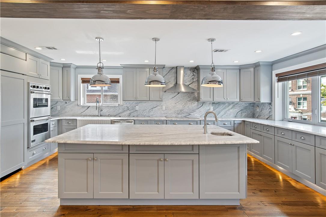 Kitchen with dark hardwood / wood-style floors, gray cabinets, wall chimney exhaust hood, decorative light fixtures, and sink