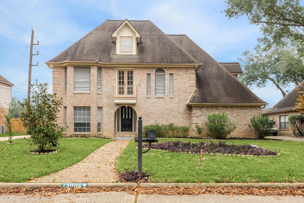 This charming two-story brick home features an arched entry and well-maintained landscaping with mature trees. A welcoming path leads to the front door, offering great curb appeal in a quiet neighborhood.