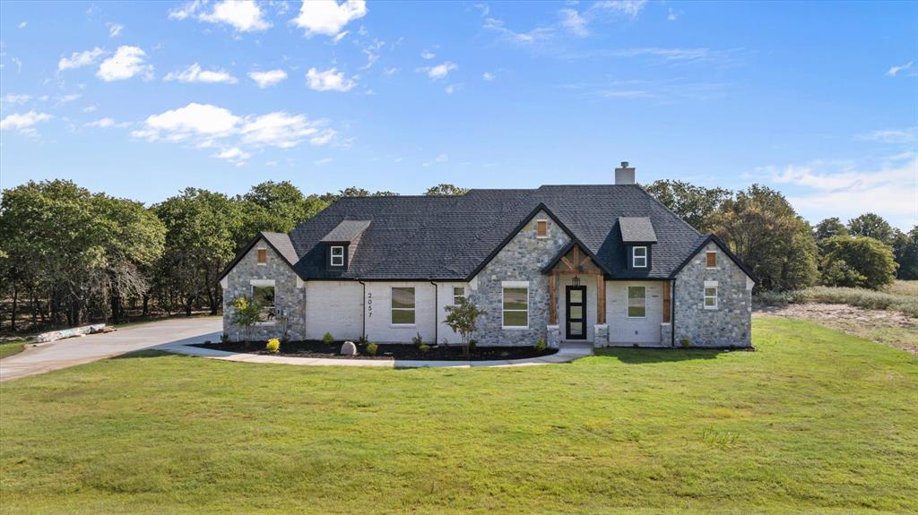 a view of a house with a big yard with plants and large tree