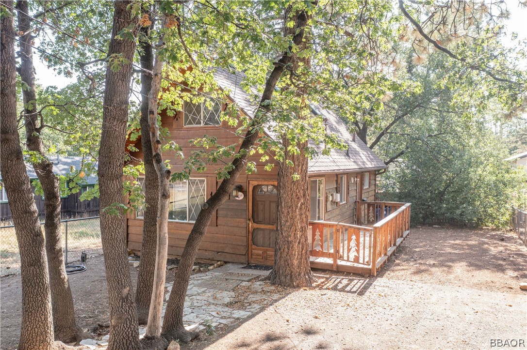 a view of a wooden house with large trees and wooden fence