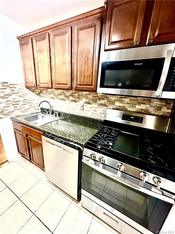 Kitchen featuring decorative backsplash, light tile patterned floors, appliances with stainless steel finishes, and sink