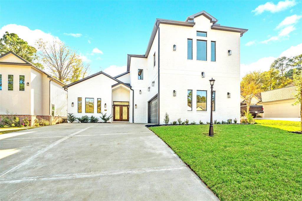 This modern contemporary masterpiece boasts a crisp white facade with bold black accents. The expansive driveway leads to a two-car garage, while the pristine front yard and lush green lawn frame the home’s elegant design.