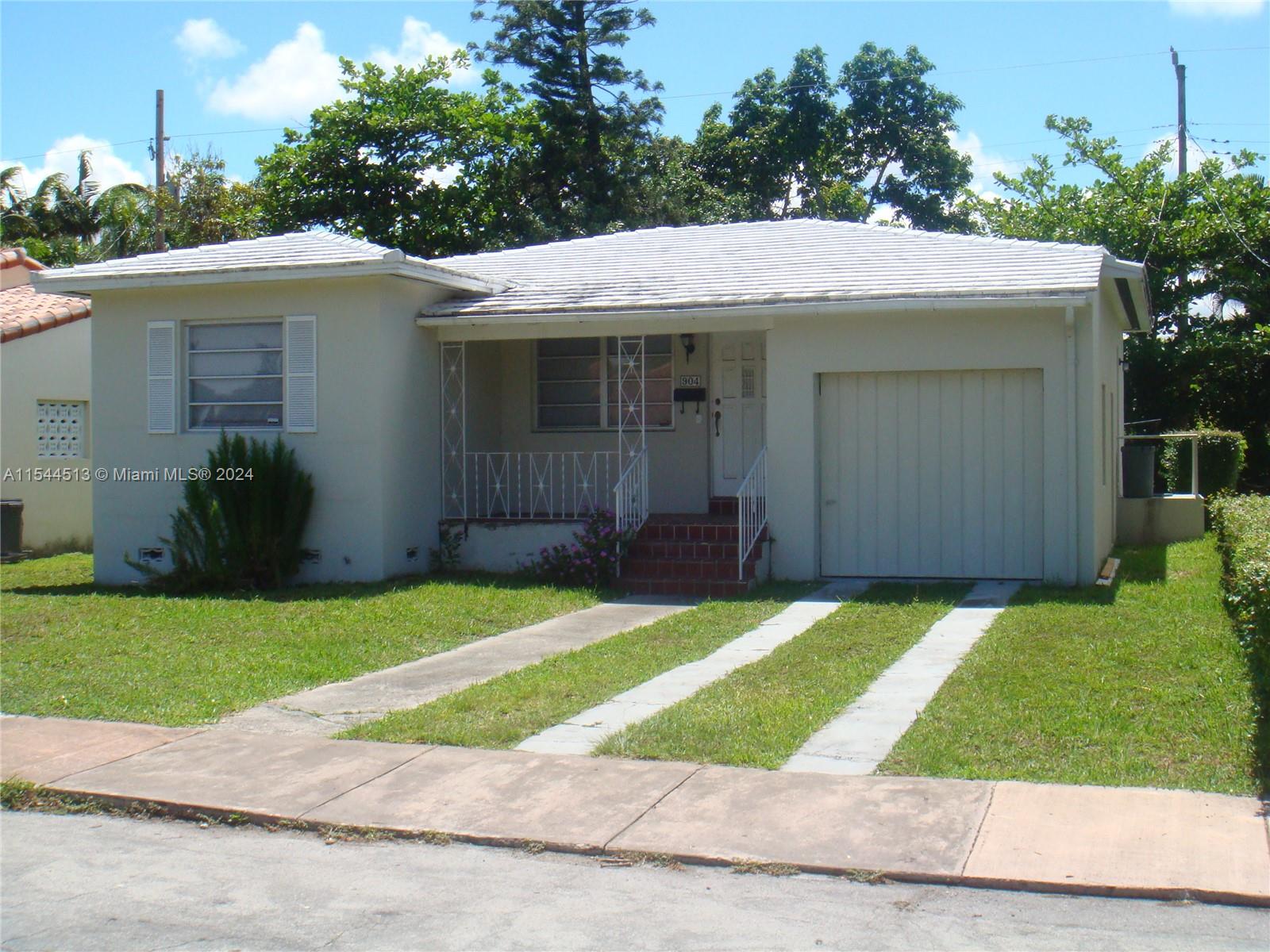 a view of a white house with a small yard plants and large tree