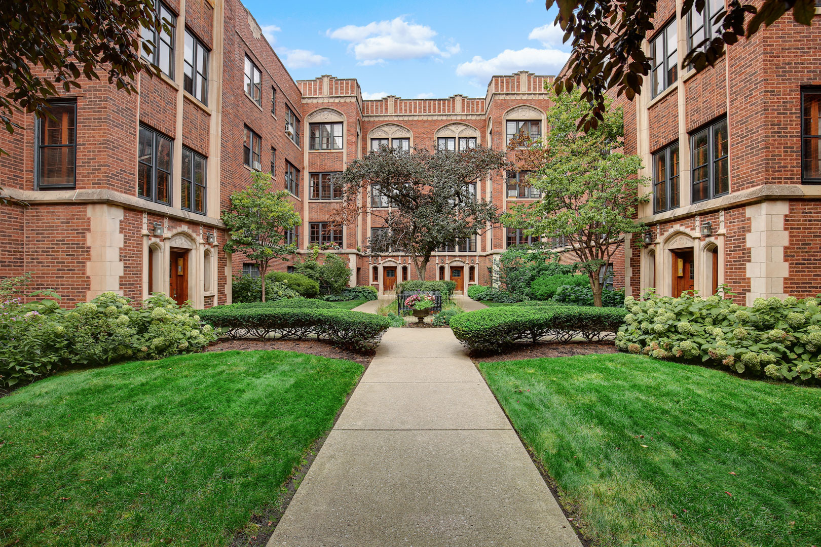 a view of a brick building next to a big yard and large trees