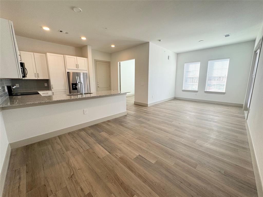 a view of a kitchen with kitchen island a sink wooden floor and stainless steel appliances