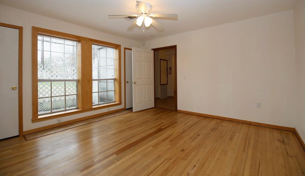 an empty room with wooden floor chandelier fan and windows