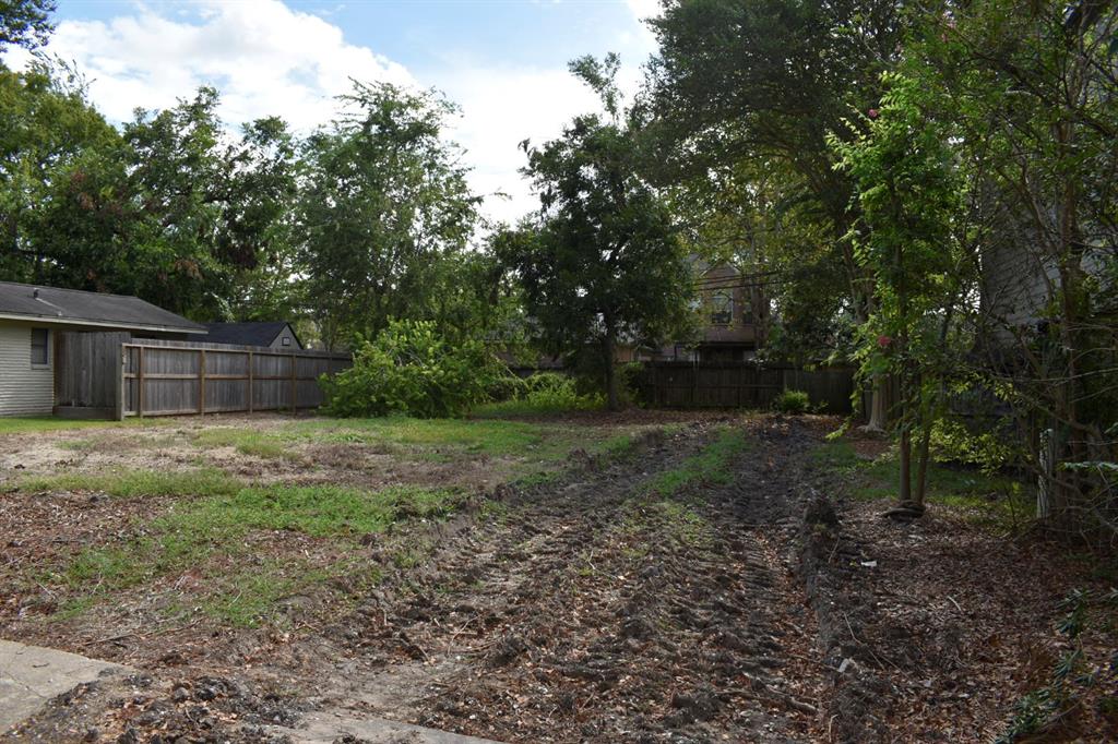 a view of a backyard with large trees and wooden fence