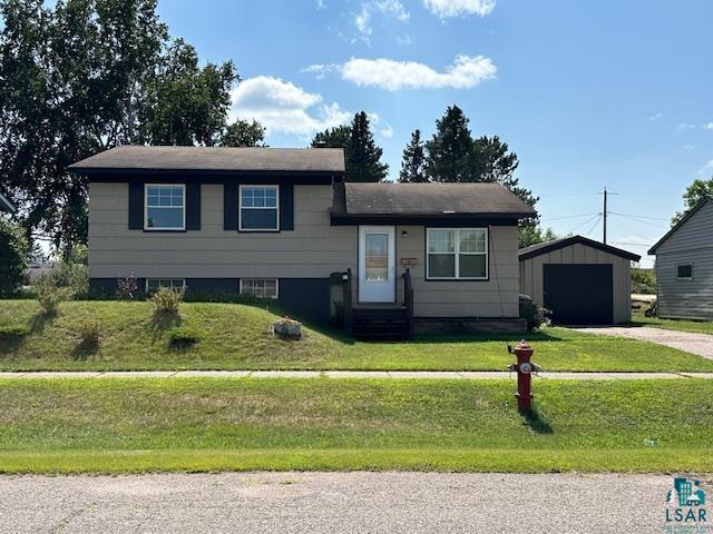 View of front of home with a garage, a front yard, and an outdoor structure