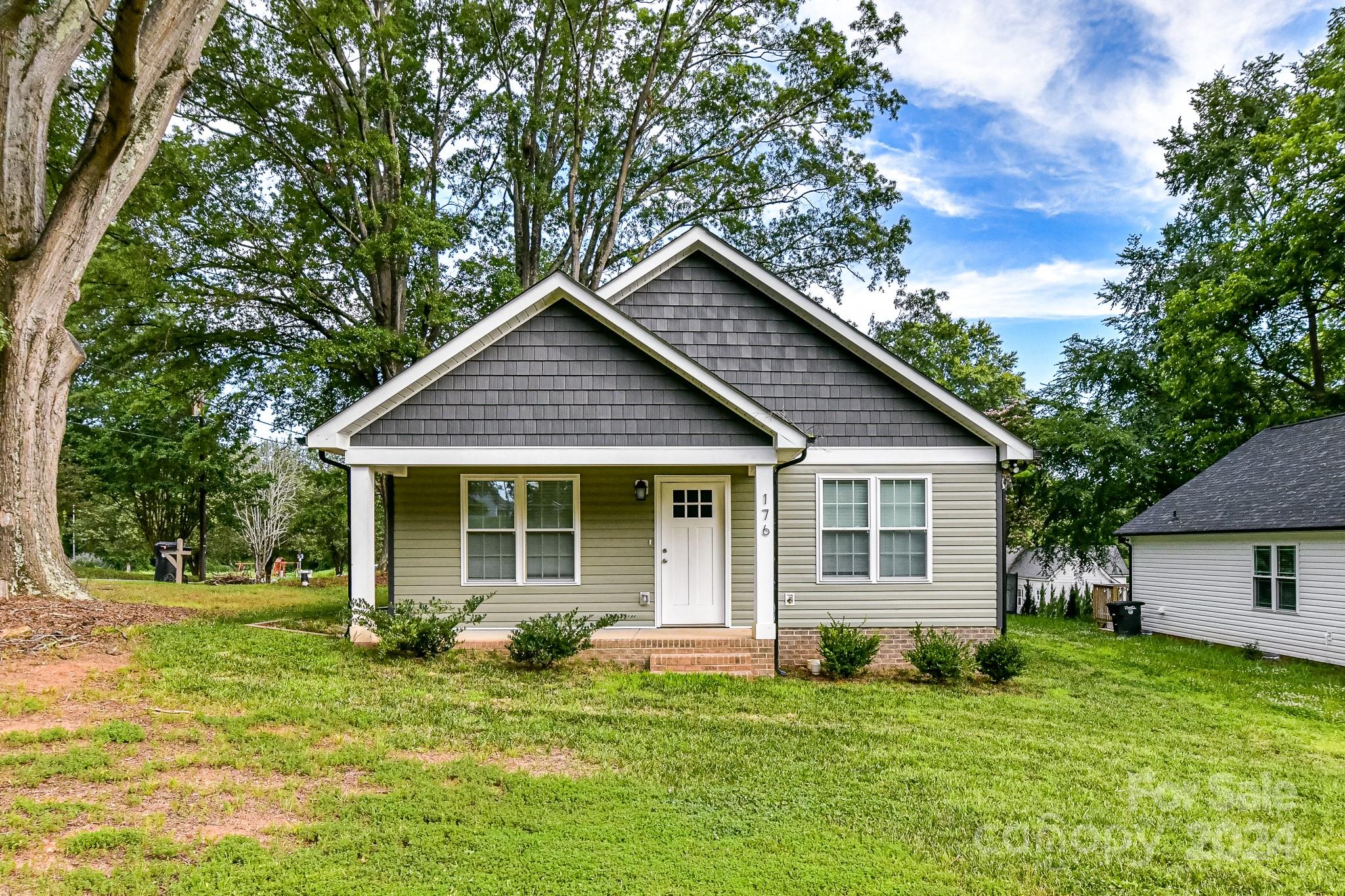 a house that is sitting in middle of grass and covered with trees