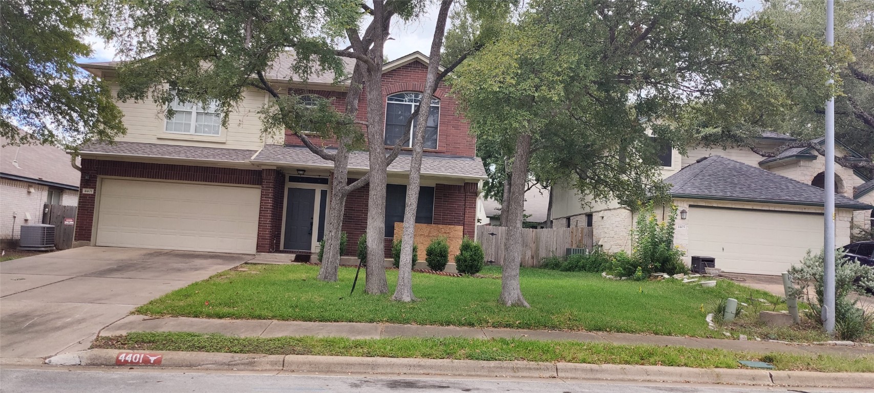 a view of a brick house with a yard plants and large tree