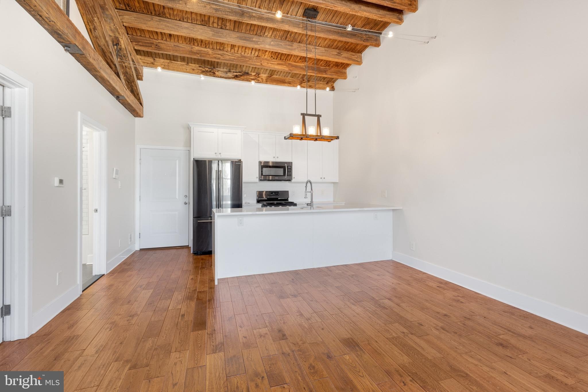 a view of empty room with wooden floor and kitchen view