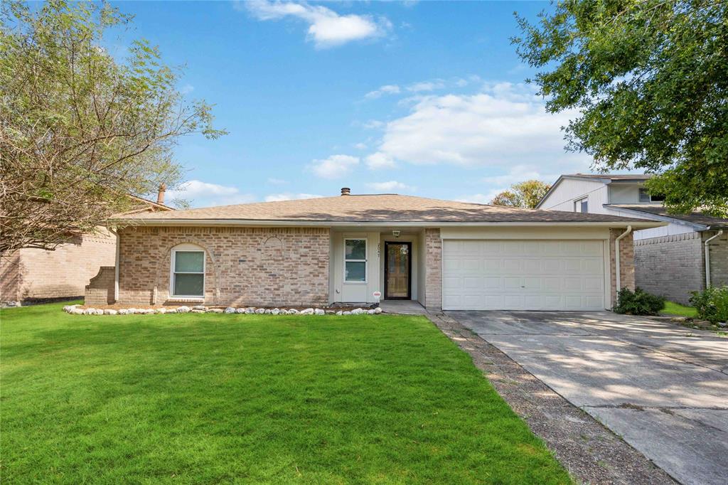 This is a single-story brick home featuring a well-maintained lawn, an attached two-car garage, and mature trees providing shade.