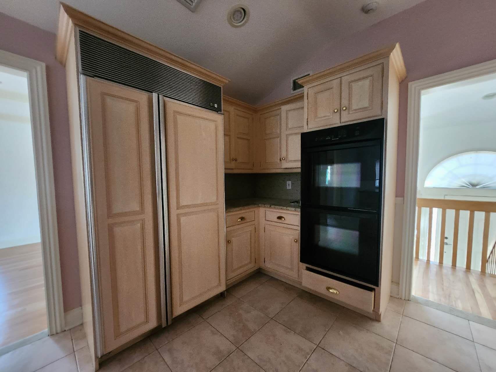 Kitchen with black double oven, paneled built in refrigerator, lofted ceiling, decorative backsplash, and light tile patterned floors