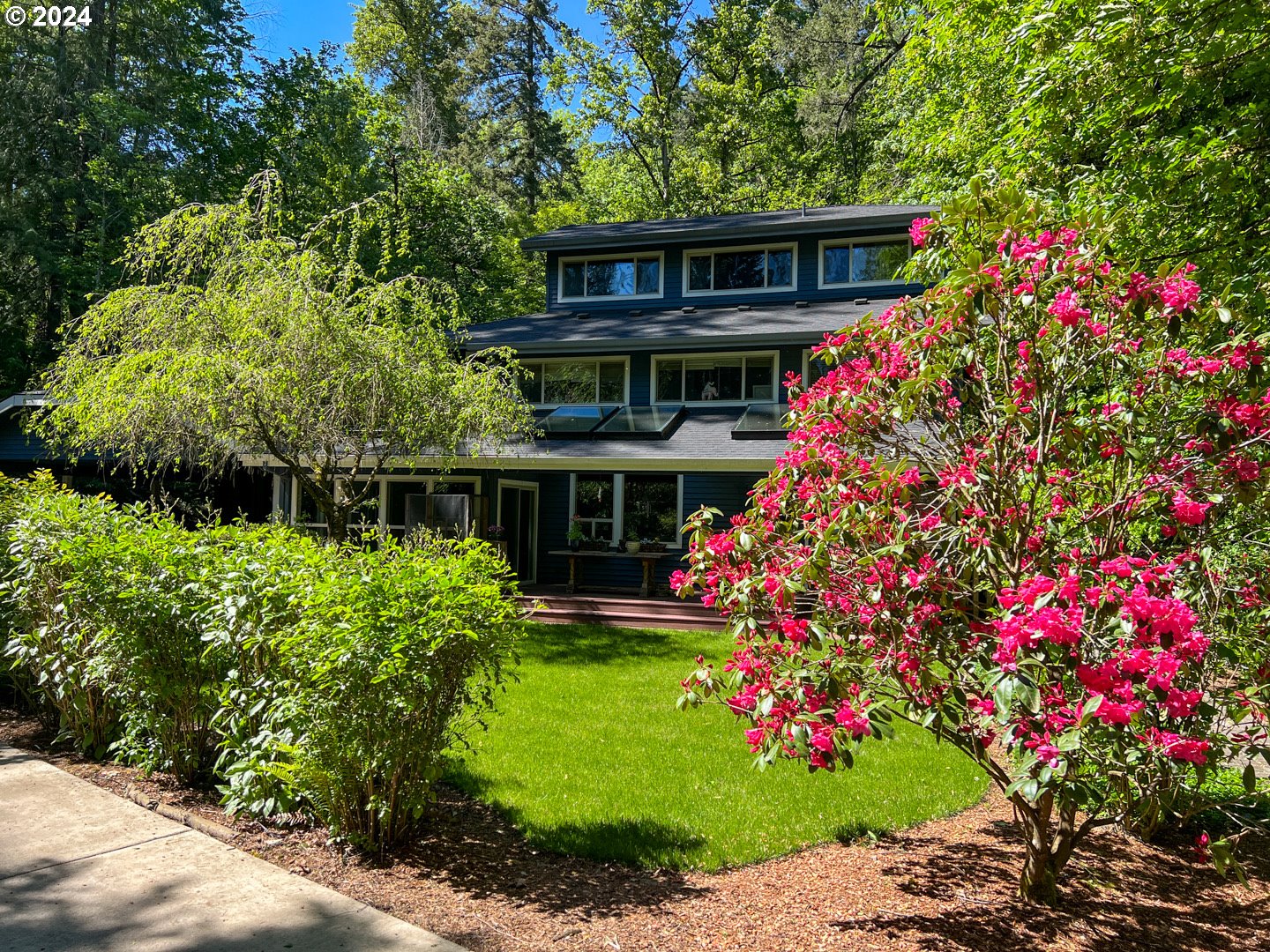 a front view of house with lot of flowers and trees