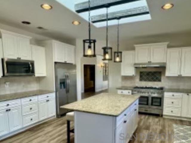 a kitchen with stainless steel appliances kitchen island granite countertop a refrigerator a sink dishwasher a stove and white cabinets with wooden floor