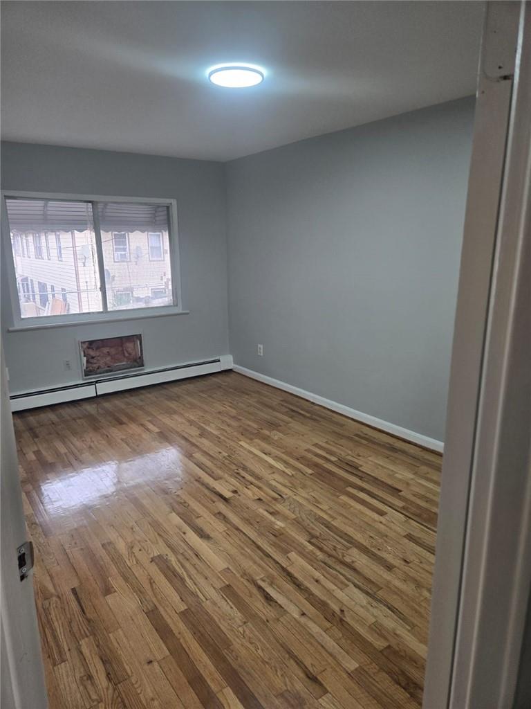 Unfurnished room featuring baseboard heating and hardwood / wood-style floors