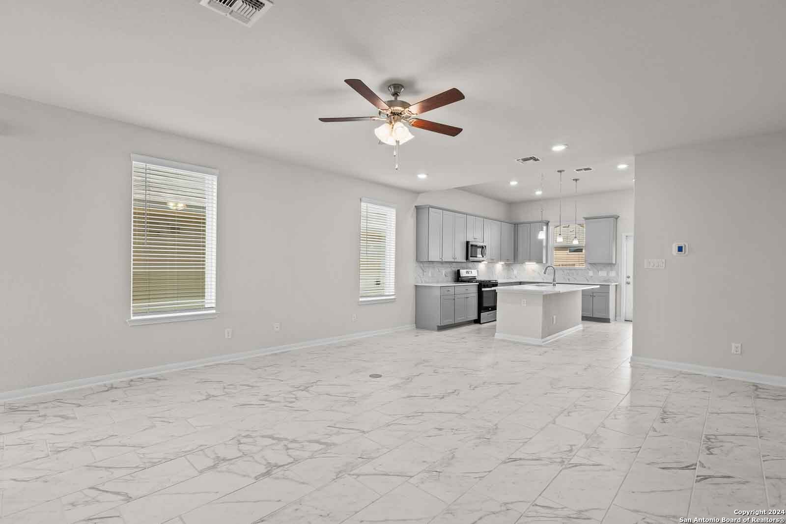 a view of an empty room with kitchen and window