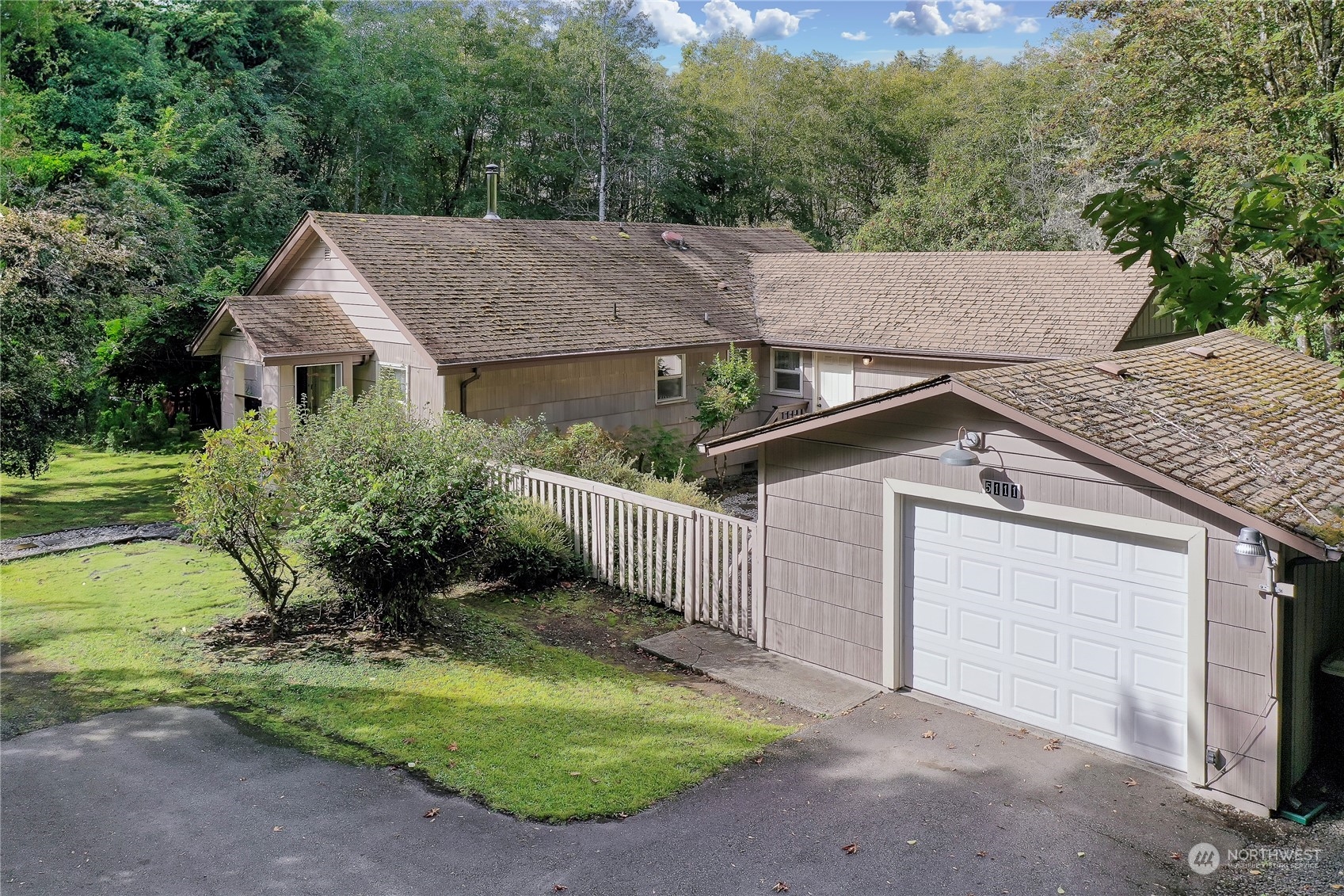 a view of a house with a yard plants and large tree