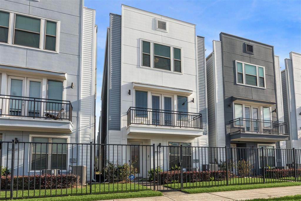 Contemporary three-story townhome with a sleek modern design, featuring a front yard, second floor balcony, and gated front yard. Ideal for urban living.