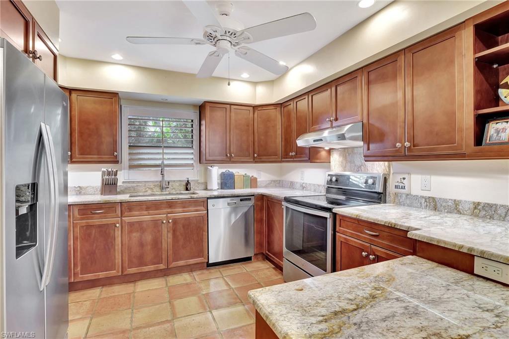 a kitchen with stainless steel appliances granite countertop a sink a stove a refrigerator cabinets and chairs