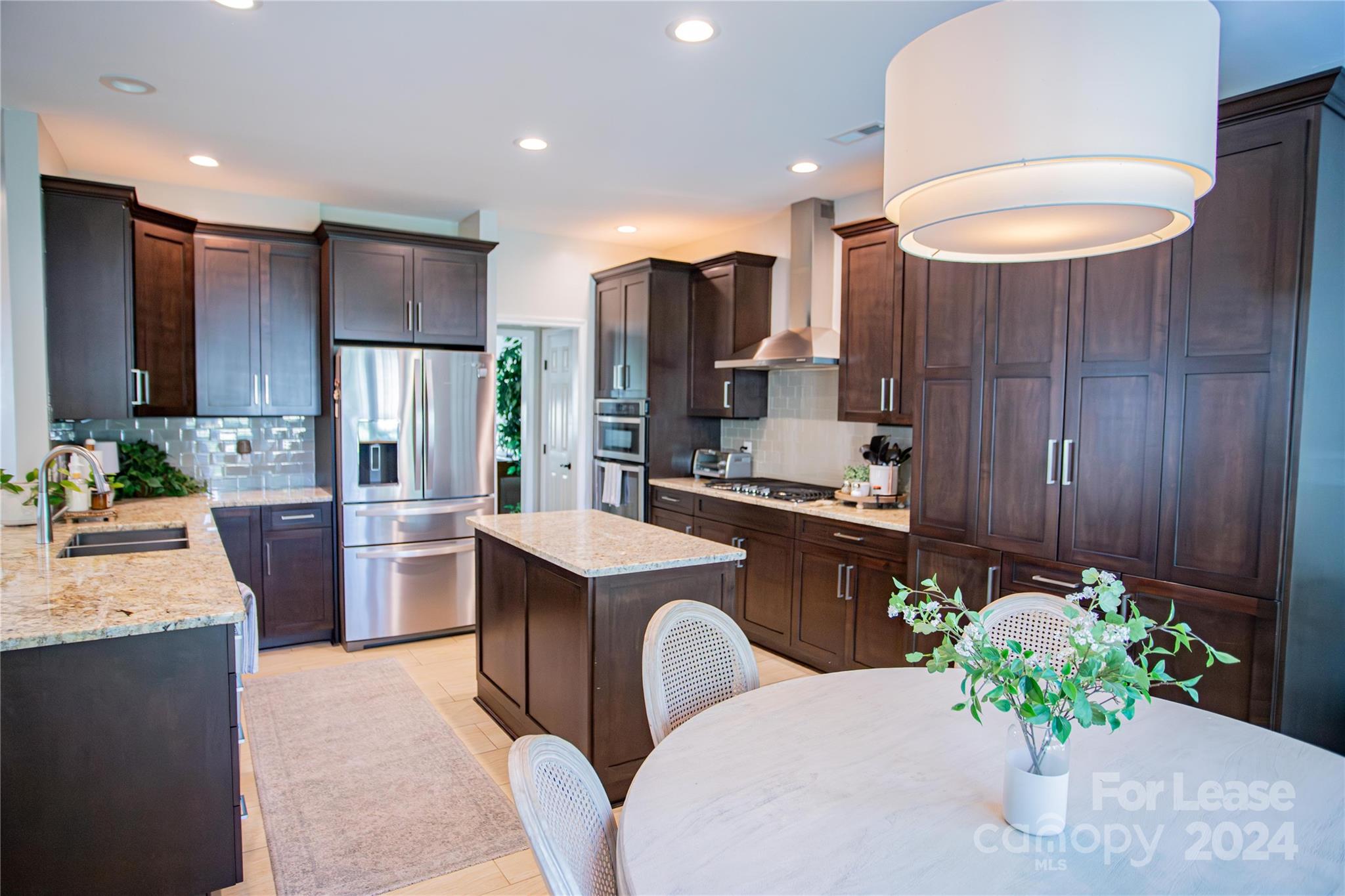 a kitchen with stainless steel appliances kitchen island granite countertop a refrigerator a sink a stove and chairs