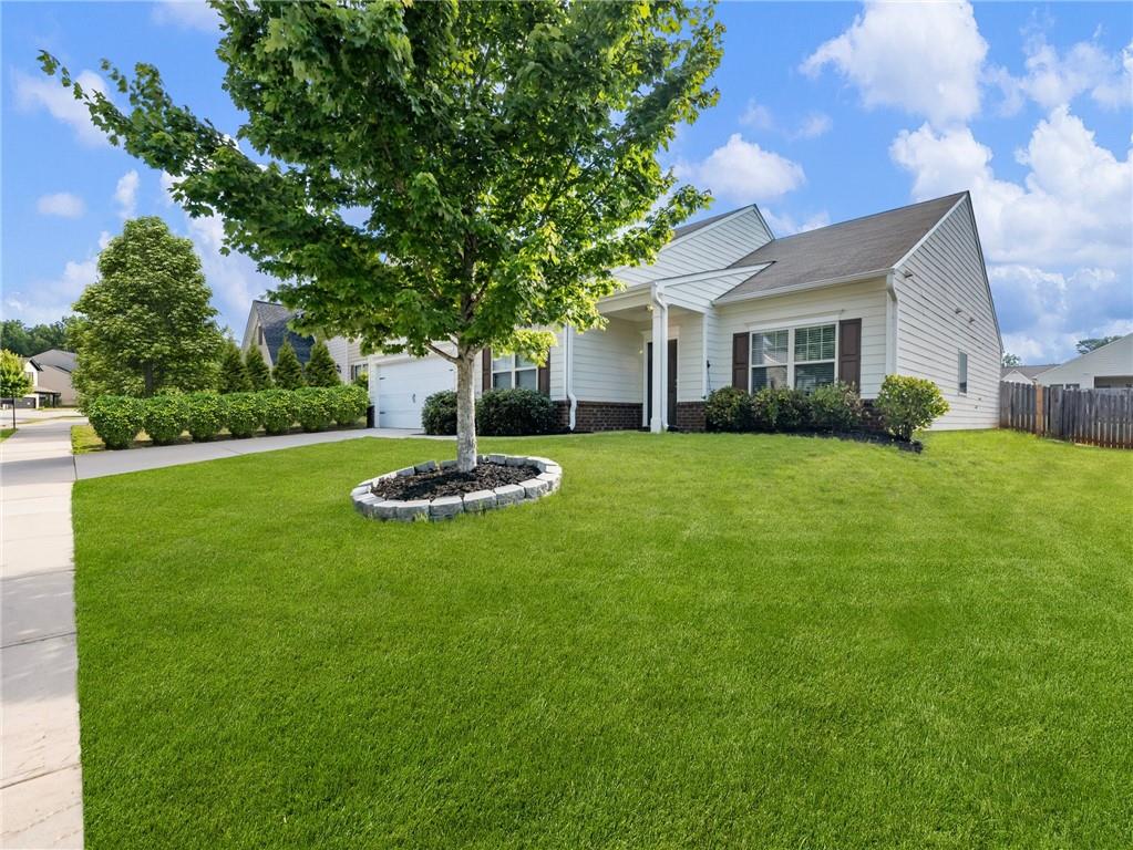 a view of a white house in front of a big yard with plants and large trees