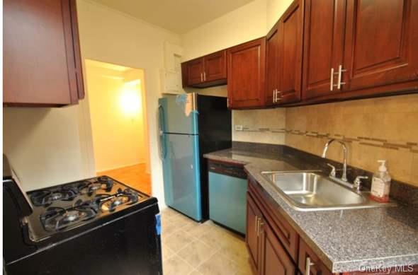 Kitchen featuring black stove, sink, stainless steel dishwasher, refrigerator, and decorative backsplash