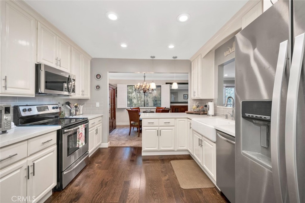 a large kitchen with stainless steel appliances granite countertop a refrigerator a stove top oven a sink dishwasher and white cabinets with wooden floor