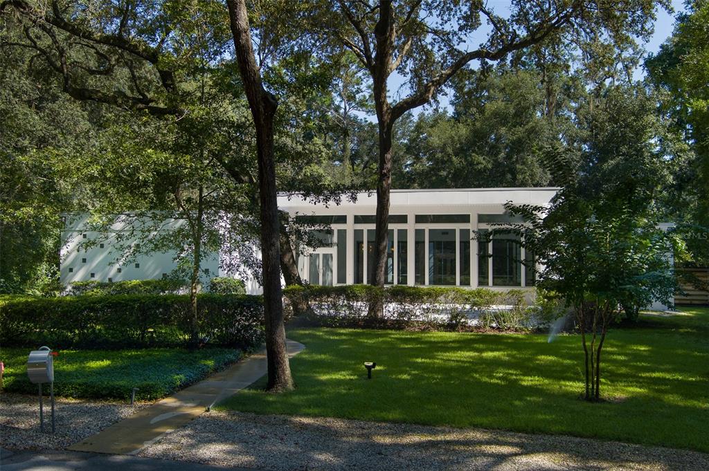 a view of a white house with a big yard and potted plants and large trees