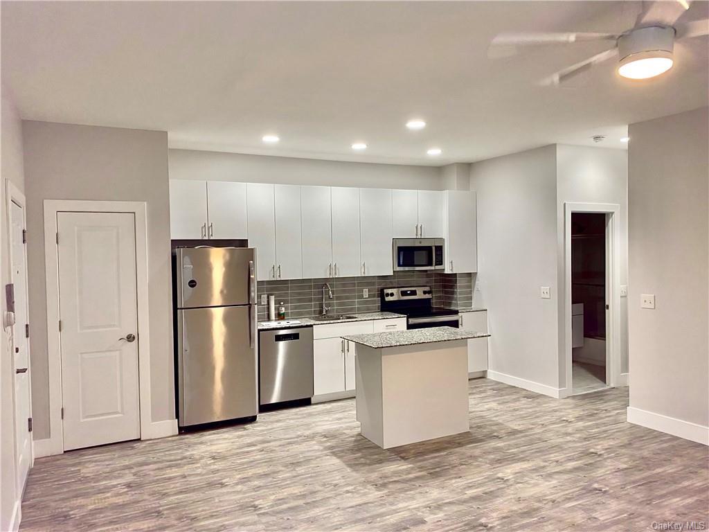 Kitchen with appliances with stainless steel finishes, white cabinetry, a kitchen island, and light hardwood / wood-style flooring