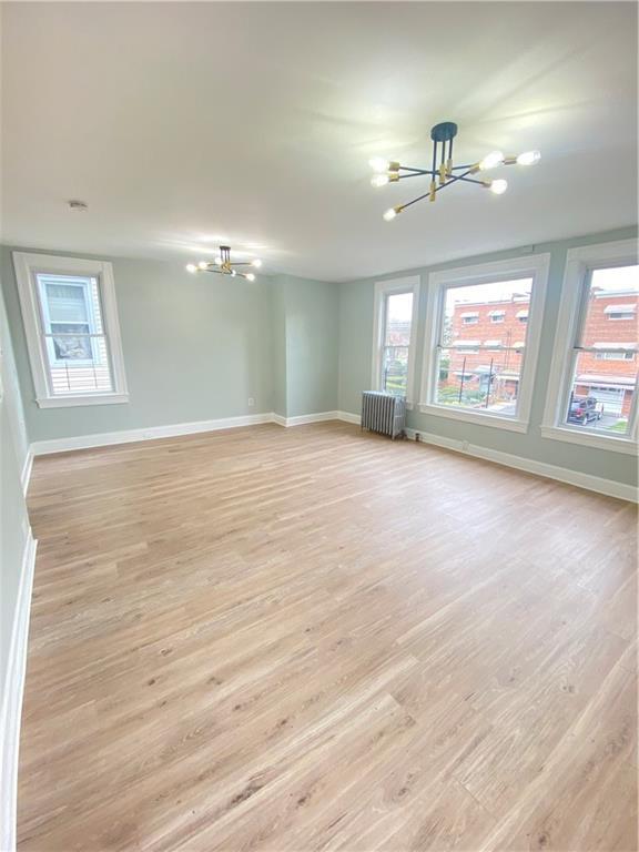 Empty room with a chandelier, light hardwood / wood-style flooring, and radiator