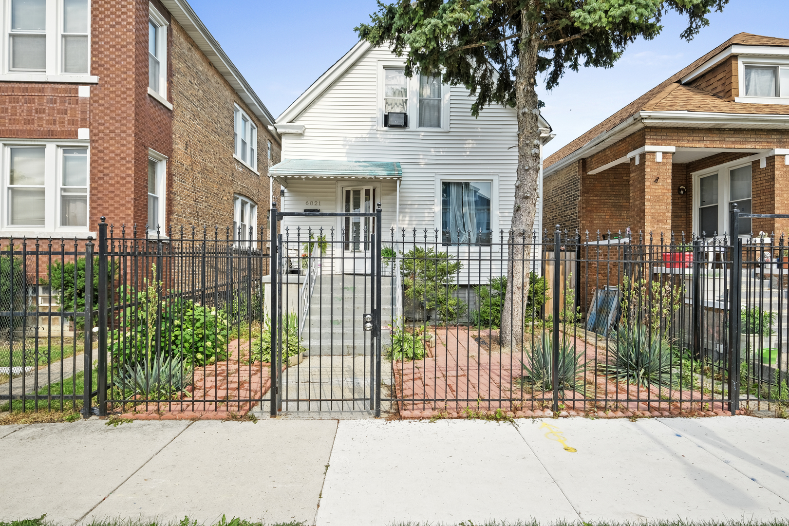 a view of a brick house with a large trees plants and wooden fence