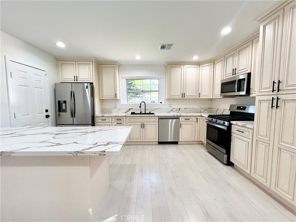 a kitchen with stainless steel appliances kitchen island granite countertop a stove a sink a refrigerator and white cabinets