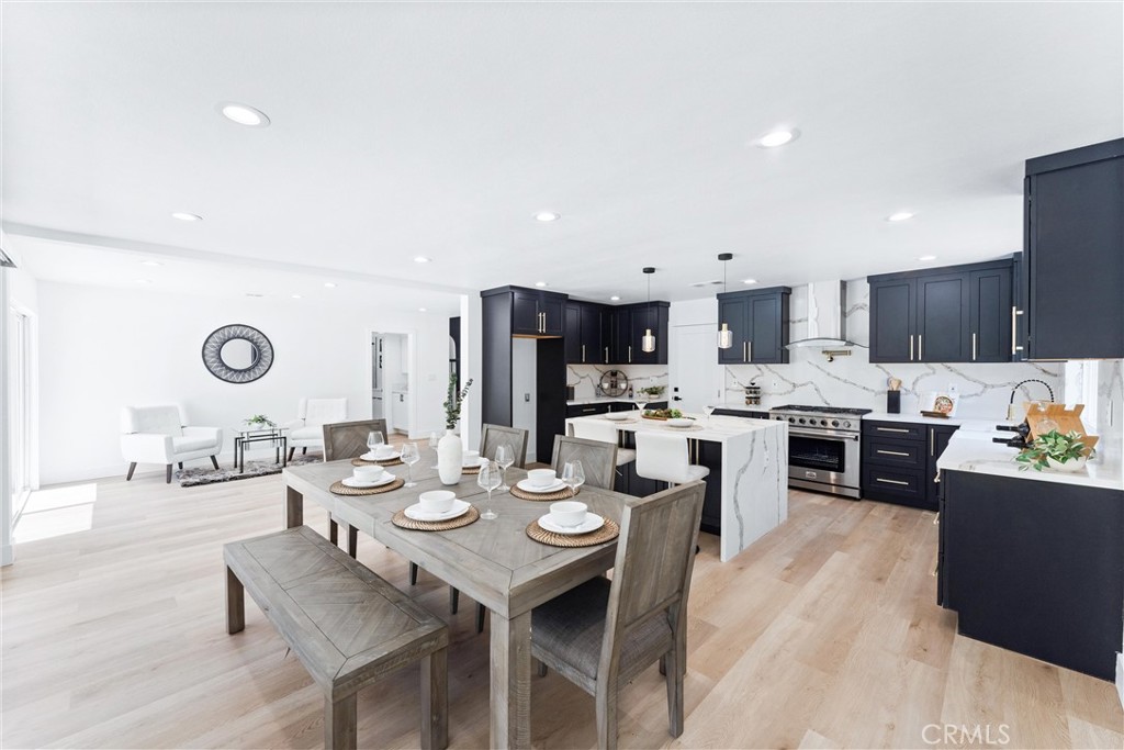 a open dining room with stainless steel appliances kitchen island granite countertop a stove a sink a dining table and chairs with wooden floor