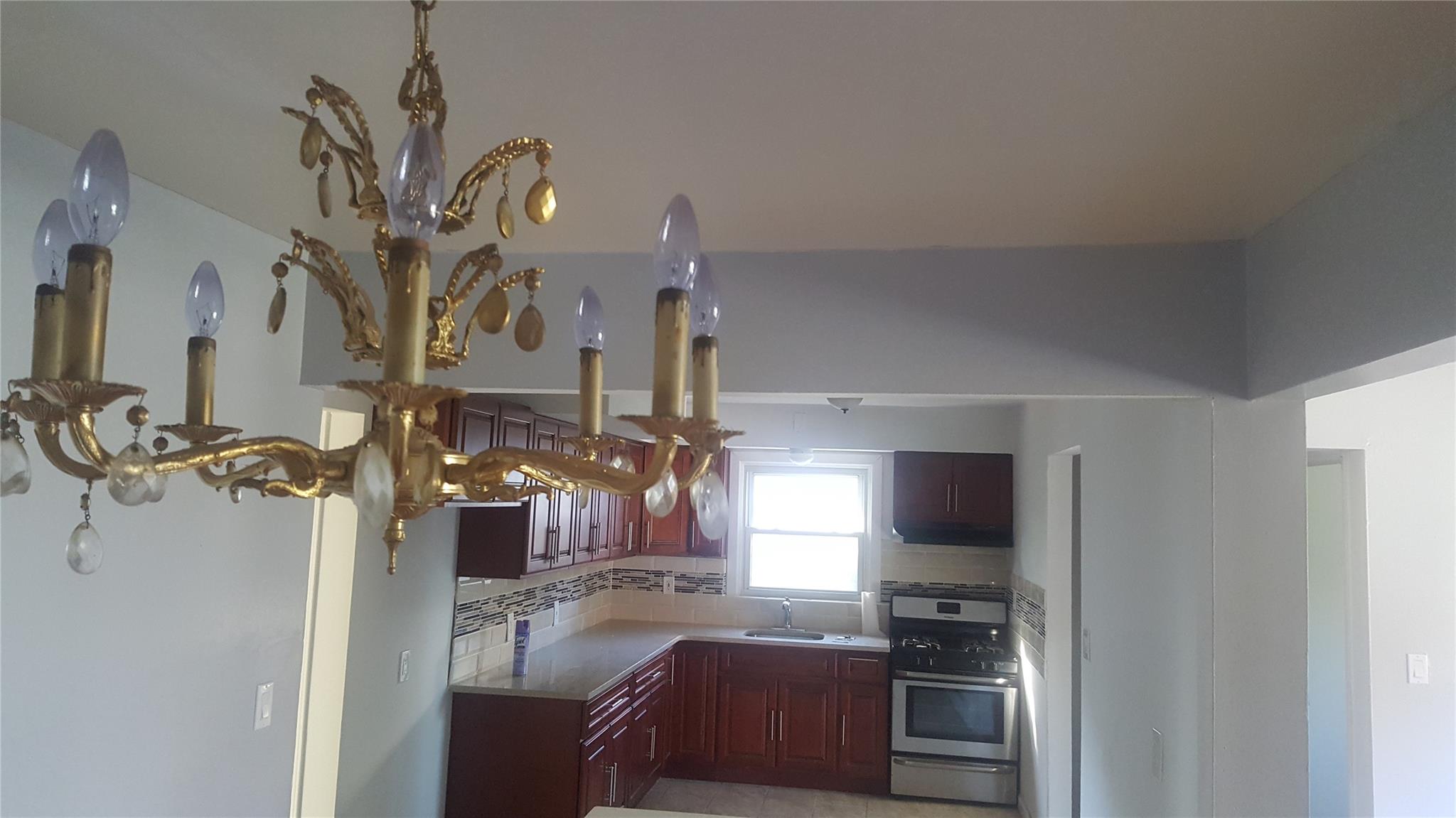 Kitchen with gas stove, backsplash, an inviting chandelier, and sink