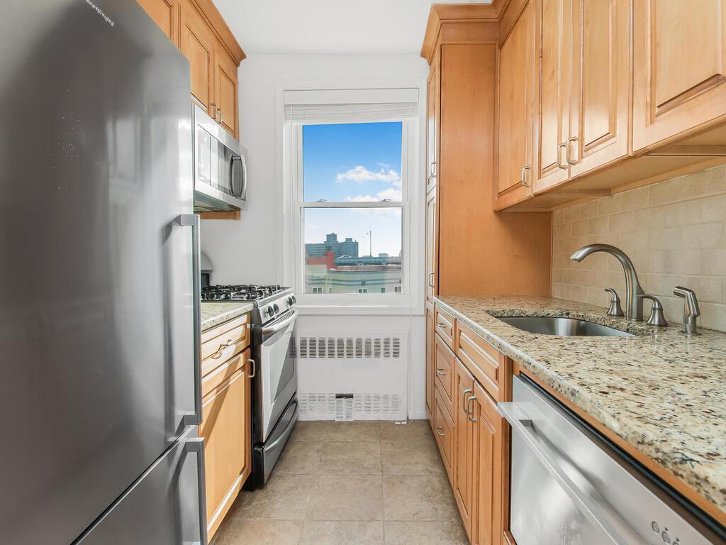 Kitchen with sink, appliances with stainless steel finishes, tasteful backsplash, light stone counters, and radiator heating unit