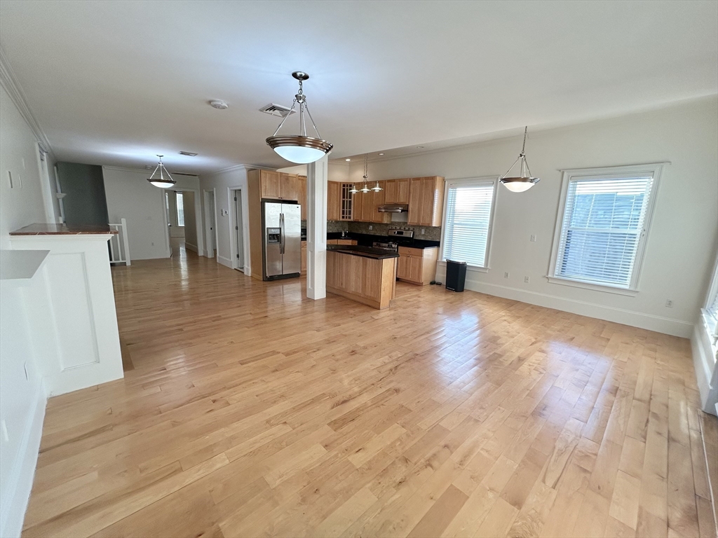 a view of a living room a kitchen island hardwood floor and a ceiling fan