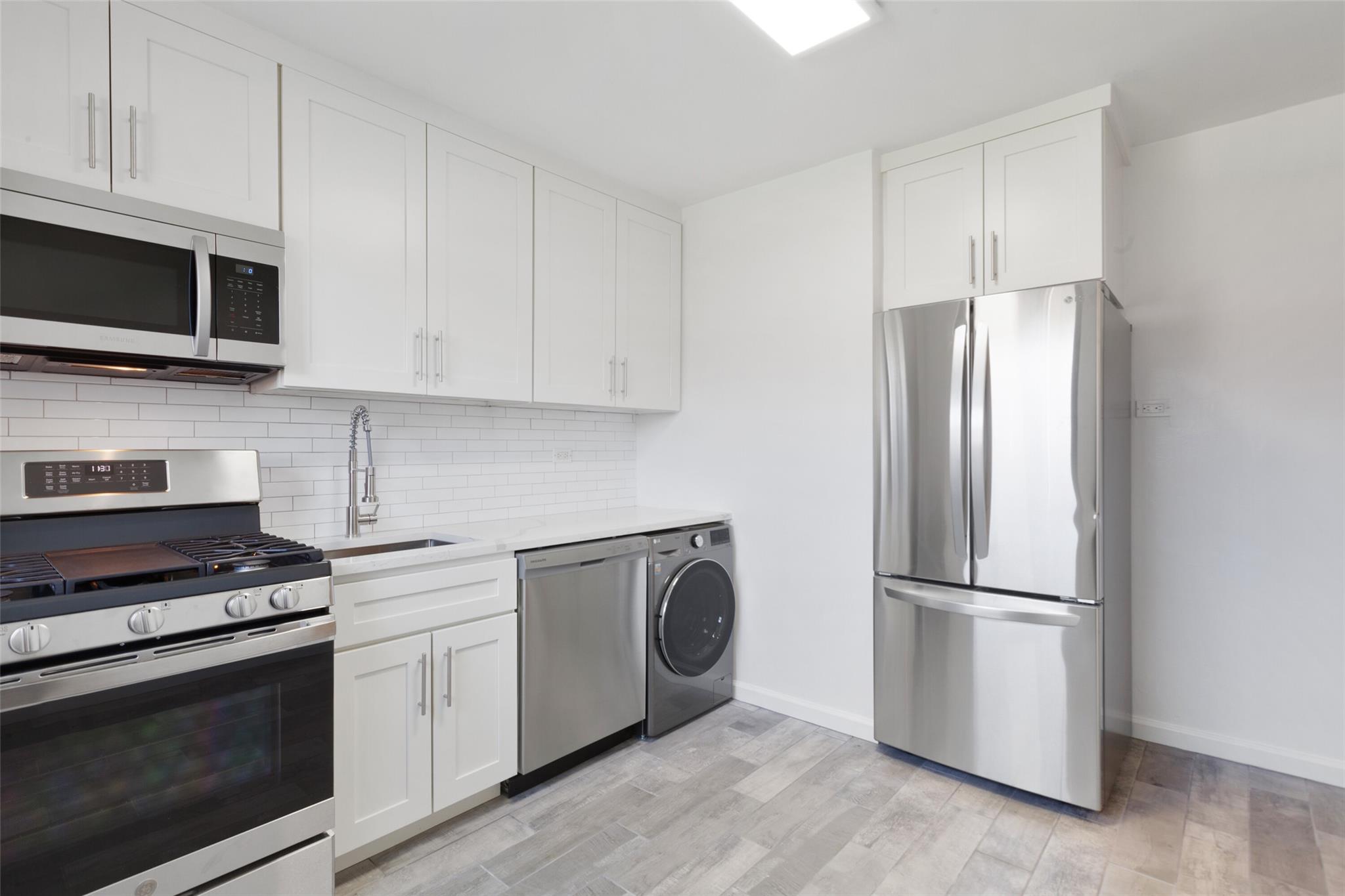 Kitchen featuring appliances with stainless steel finishes, sink, light ceramic tile/ wood-style flooring, washer / clothes dryer, and white cabinetry