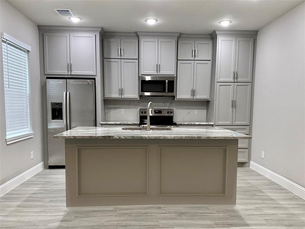 a kitchen with stainless steel appliances granite countertop a stove a refrigerator a sink a microwave oven with white cabinets and wooden floor