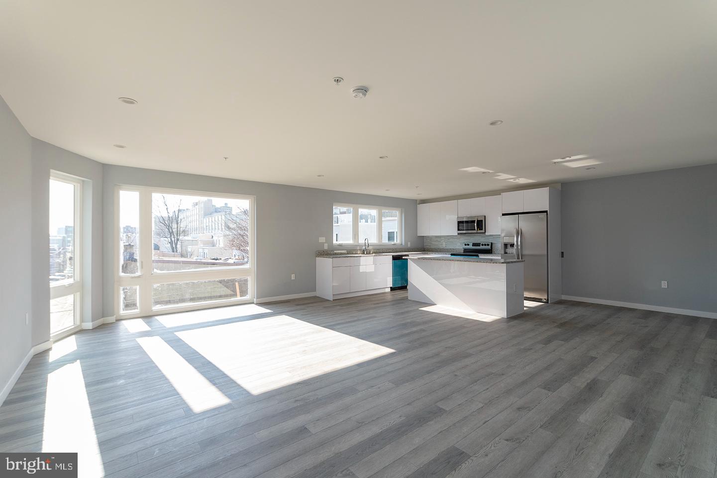 a view of empty room with wooden floor and kitchen view