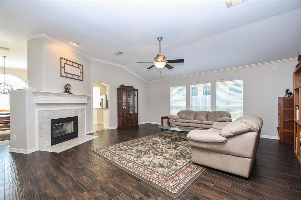 This is a spacious and well-lit living room featuring wood-look tile floors, a classic white, two-way fireplace, large windows with blinds, and neutral walls.