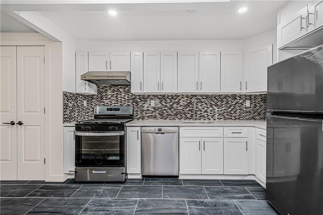 Kitchen featuring white cabinets, stainless steel appliances, wall chimney exhaust hood, dark tile patterned flooring, and sink