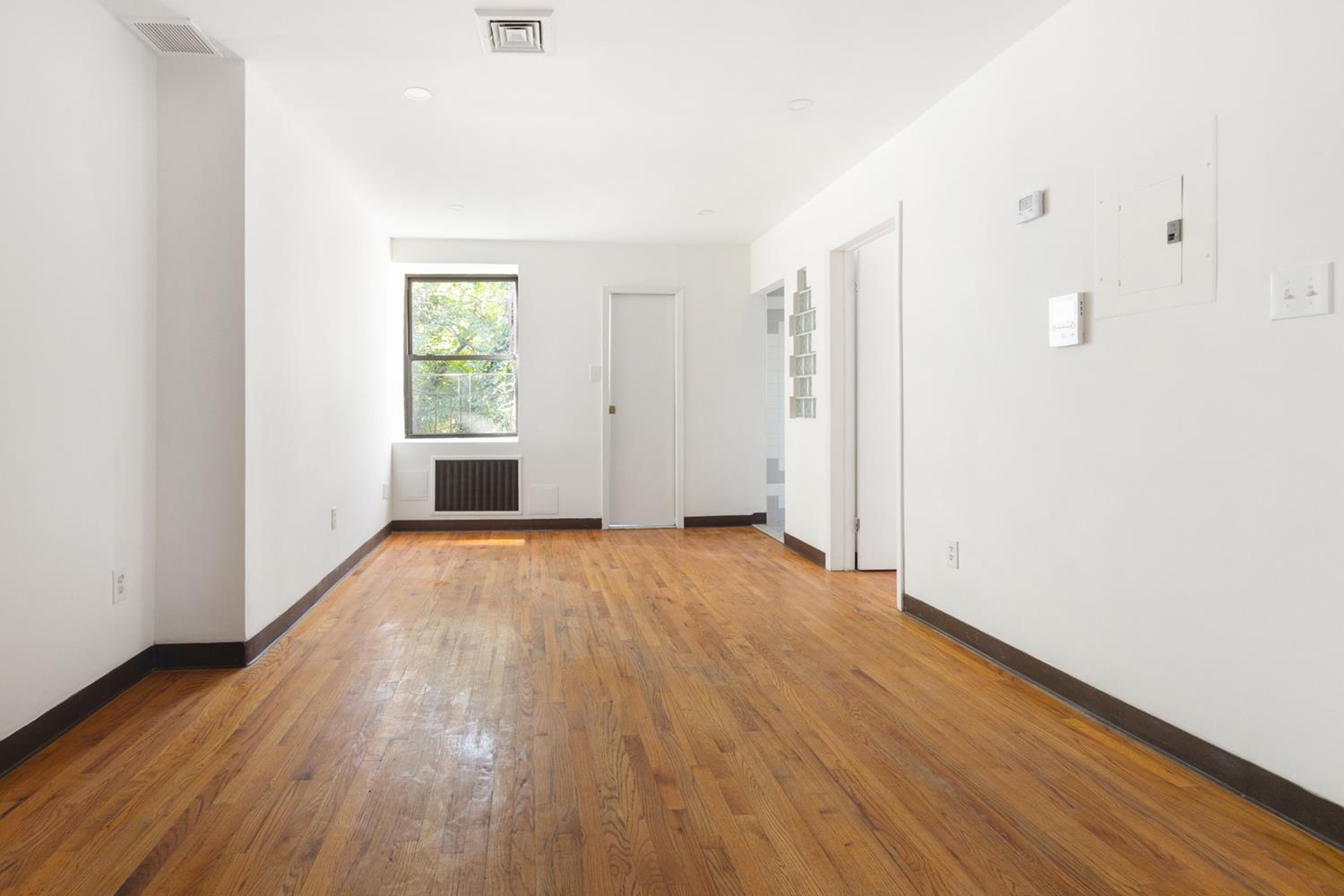 a view of an empty room with wooden floor and a window